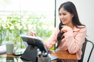 Modern işyerinde otururken dijital ortamda çalışan kadın girişimci. Tablet üzerinde dokunmatik kalem kullanan kadın. .