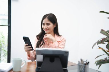 Genç meşgul Asyalı iş kadını lideri cep telefonu kullanıyor, akıllı telefona bakıyor modern şirket ofisinde çalışan finans piyasası uygulamasını kontrol ediyor. .