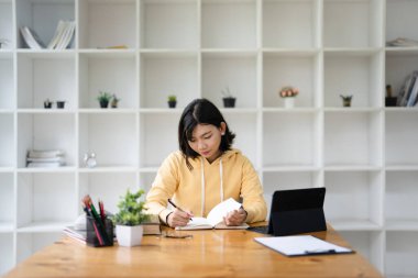 Not defterine kalem yazan ve ofis masasında dizüstü bilgisayarlı bir kadın. Öğrenci çevrimiçi ders çalışıyor ve not alıyor, e-öğrenme, iş etkinliği planlama, liste hatırlatması yapmak için