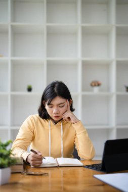 Düşünceli Asyalı kadın serbest çalışıyor. Bilgisayarlı akıllı telefon kullanıyor. İçerideki rahat iç mekanlara karşı mesafeli pozlar veriyor. Kadın dijital göçebe modern yaşam tarzını seviyor