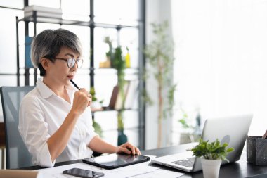 İş yerindeki kadın patron, kıdemli beyaz saçlı iş kadını tablet bilgisayar kullanıyor, mali verileri kontrol etmekten mutlu, dizüstü bilgisayarlı bankacı kadın..