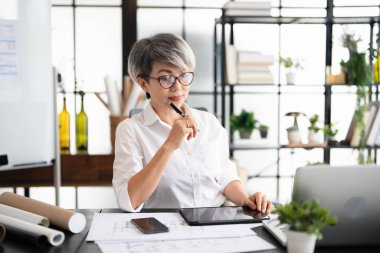 Kendine güvenen yaşlı bir kadın, modern ofiste çalışan dizüstü bilgisayarı kullanan bir yönetici. Şık gözlükler takan iş kadını e-postaları kontrol ediyor. Teknoloji konsepti