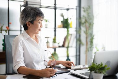 Modern konsantre iş kadını muhasebeci elinde gözlüklerle belgeleri analiz ediyor, bilgisayarla evden çalışıyor. Kadın çek ödemeleri, hesap makinesine güvenin. Yaşlılar ve serbest meslek anlayışı