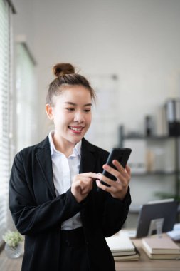 Genç, meşgul bir iş kadını modern ofiste telefonla konuşuyor. Asyalı iş kadını şirket satış müdürü takım elbise giyiyor cep telefonuyla arama yapıyor iş yerinde duruyor.