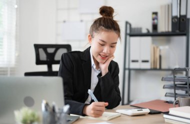 Masasında çalışan genç Asyalı kadın, notlar yazıyor. İş kadını iş yerinde..