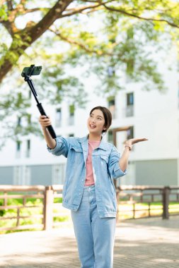 Şehirdeki turistler üniversite caddesinde selfie çekiyor. Asyalı kız yazın sokaklarda cep telefonuyla mutlu mesut yürürken selfie çekiyor. Seyahat ve yaz tatili yaşam tarzı kavramı.