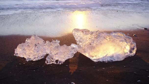 日没時に黒い火山砂に輝く氷山 波に衝突した氷の塊 アイスランドの有名なダイヤモンドビーチ 8K解像度で撮影 — ストック動画