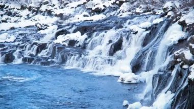 Waterfall in Iceland, Snowy Mountain and Cold River in Winter. Magical Outdoor Winter Time Location, Blue Glacial Water with a Huge Current. Pure Scenic Landscape. Hraunfossar. Shot in 8k Resolution.