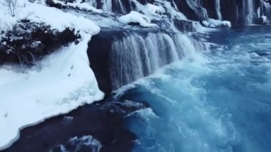 Waterfall in Iceland, Snowy Mountain and Cold River in Winter. Magical Outdoor Winter Time Location, Blue Glacial Water with a Huge Current. Pure Scenic Landscape. Hraunfossar. 