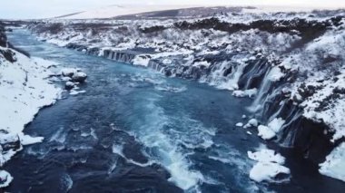 Waterfall in Iceland, Snowy Mountain and Cold River in Winter. Magical Outdoor Winter Time Location, Blue Glacial Water with a Huge Current. Pure Scenic Landscape. Hraunfossar. 