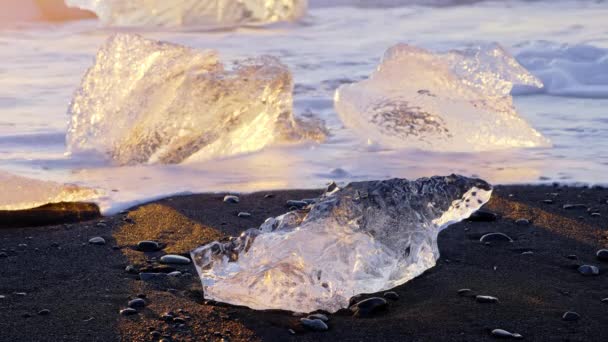 アイスランドの有名なダイヤモンドビーチ 日没時に黒い火山の砂に輝く氷山 オーシャン ウェーブに衝突した透明な氷 8K解像度で撮影 — ストック動画