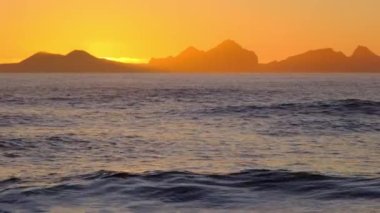 Fırtınalı Deniz 'de gün doğumu. Sunset 'te Parlayan Altın Dalgalar ve Güneş Yansıması. İzlanda kıyı şeridinde inanılmaz bir ışık var. Keskin Volkanik Uçurumlar. İzlanda. Çekim 8K Çözüm 4320p.