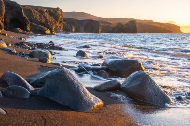 Scenic beach with black sand by low tide at sunset, Sharp mountain volcanic cliffs on Atlantic ocean coastline, Famous touristic place in Iceland. High quality photo