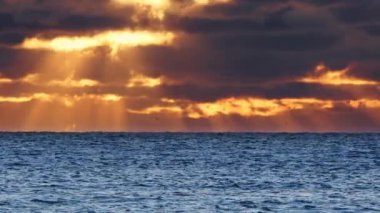 Dramatik deniz batımı. Yanan gökyüzü ve parlayan dalgalar. Güneş doğarken sıcak bulutlar ve saf okyanus suyu. Mavi ve turuncu renkler. Doğa sineması sahnesi 8K çözünürlükte 4320 peni. Yüksek kalite 4k görüntü
