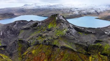 Dağ gölünde turkuaz su. Mavi Göl 'ün havadan görünüşü ve İzlanda' daki volkanik dağlar. Baharda yeşil yosun ve beyaz karlı İzlanda manzarası. Destansı hava manzarası. 4k