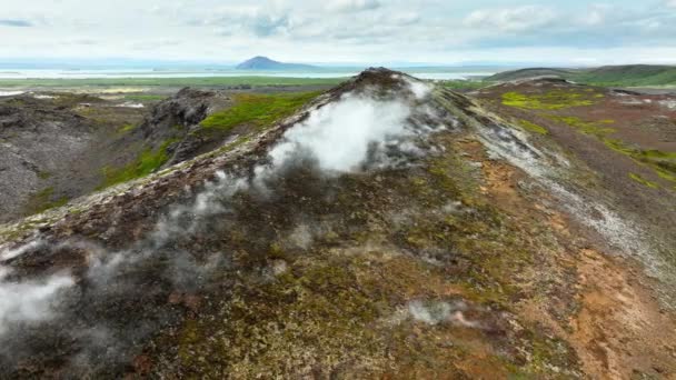 湖の近くの地熱地帯 Myvatn Smoky Hill自然の中でアイスランドの煙夏の晴れた日に山の頂上から立ち上がる火山活動マグマ地球の空中ビューの下で 高品質4K映像 — ストック動画