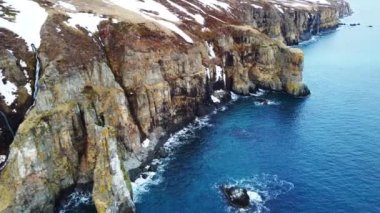 Kayalık sahil şeridinde uçuyor. Bahar mevsiminde İzlanda 'da kuzey Atlantik' in mavi okyanus suyunda kar yağışı ile uçurumun kenarında. Hava görüntüsü 4K