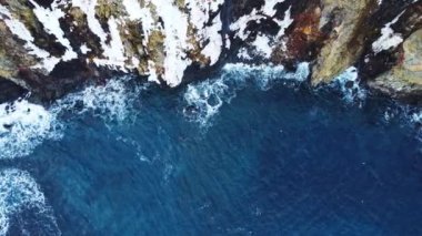 Kayalık sahil şeridinde uçuyor. Bahar mevsiminde İzlanda 'da kuzey Atlantik' in mavi okyanus suyunda kar yağışı ile uçurumun kenarında. Hava görüntüsü 4K