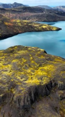 Dikey Ekran: Su Bulutları Yansıtan Dağ Gölü, İzlanda Doğası. Baharın başlarında Lav Tarlaları Sarı Yosun ile kaplıydı. Manzaralı Epic Aerial View Manzarası, Sosyal Medya Çekimi. 4k.