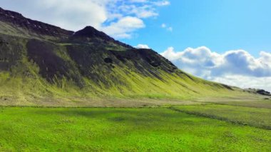 İzlanda 'daki manzara manzarası. Baharda yeşil çimenli dağlar. Dağların üzerinde bulutlu mavi gökyüzü. Sakin ve güneşli bir günün arka planı. Kırsal bölgede hava manzarası. 4k