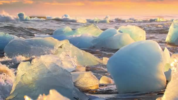 黄金の時間に黒いビーチで輝くアイスバーグ アイスランドのダイヤモンドビーチで日の出 海の波に衝突した氷 気候変動 地球温暖化問題 高品質の4K映像 — ストック動画