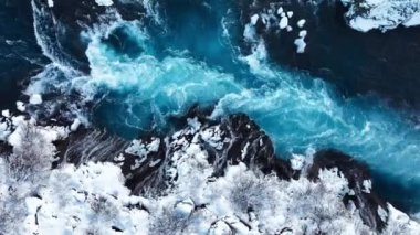 İzlanda 'da şelale, kışın soğuk nehri olan karlı dağ, kar ve buzun büyülü yeri, büyük akıntılı mavi buzul suyu. Saf Manzara Manzarası. Hraunfossar. 4k görüntü