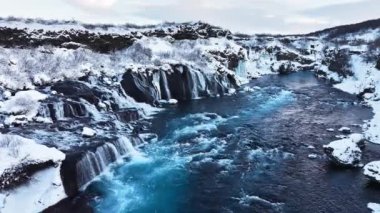 İzlanda 'da şelale, kışın soğuk nehri olan karlı dağ, kar ve buzun büyülü yeri, büyük akıntılı mavi buzul suyu. Saf Manzara Manzarası. Hraunfossar. 4k görüntü