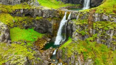 İnce şelaleler uçurumdan aşağı akıyor, dağ nehri uçurumdan düşüyor İzlanda 'da yeşil bitki örtüsü ile birçok şelale oluşturuyor. Yüksek kalite 4k görüntü