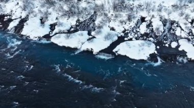 İzlanda 'da şelale, kışın soğuk nehri olan karlı dağ, kar ve buzun büyülü yeri, büyük akıntılı mavi buzul suyu. Saf Manzara Manzarası. Hraunfossar. 4k görüntü