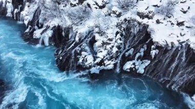 İzlanda 'da şelale, kışın soğuk nehri olan karlı dağ, kar ve buzun büyülü yeri, büyük akıntılı mavi buzul suyu. Saf Manzara Manzarası. Hraunfossar. 4k görüntü
