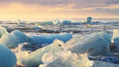 Altın saat boyunca siyah bir sahilde parlayan buzdağları. İzlanda 'da Diamond Sahili' nde gün doğumu. Temiz buz okyanus dalgaları tarafından çarpıldı. İklim Değişimi Küresel Isınma sorunu. Yüksek kalite 4k görüntü