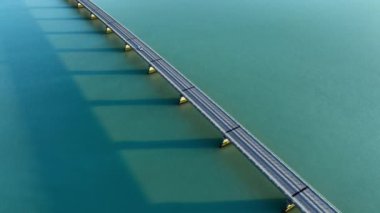 Turkuaz su üzerindeki köprü, köprüde giden bir arabanın hava aracı görüntüsü, etkileyici şehir altyapısı, simetrik hatlar ve okyanus suyunun üzerindeki gölgeler. Yüksek kalite 4k görüntü
