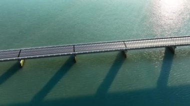 Turkuaz su üzerindeki köprü, köprüde giden bir arabanın hava aracı görüntüsü, etkileyici şehir altyapısı, simetrik hatlar ve okyanus suyunun üzerindeki gölgeler. Yüksek kalite 4k görüntü