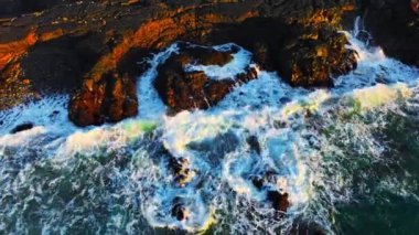 Atlantik Okyanusu kıyıları rüzgarlı havada, büyük dalgalar keskin siyah bazalt kayalara vuruyor, gün batımında İzlanda kıyıları, açık denizlerde fırtına. Yüksek kalite 4k görüntü