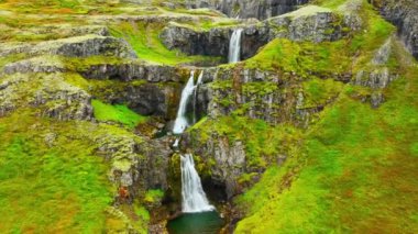 İnce şelaleler uçurumdan aşağı akıyor, dağ nehri uçurumdan düşüyor İzlanda 'da yeşil bitki örtüsü ile birçok şelale oluşturuyor. Yüksek kalite 4k görüntü