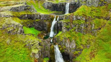 İnce şelaleler uçurumdan aşağı akıyor, dağ nehri uçurumdan düşüyor İzlanda 'da yeşil bitki örtüsü ile birçok şelale oluşturuyor. Yüksek kalite 4k görüntü