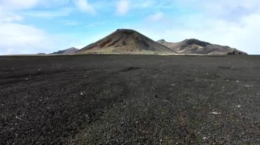 Siyah volkanik çöl, kara kum üzerinde insansız hava aracı uçuşu, arka planda sönmüş eski bir volkan. Yüksek kalite 4k görüntü