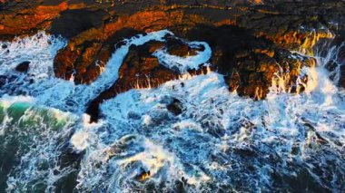 Okyanus dalgalarının yukarıdan görünüşü muhteşem kayaların ve kayalıkların etrafında köpürüyor. İlham verici ve inanılmaz doğa konsepti. Destansı sahil şeridinde güçlü deniz suyunun insansız hava aracı çekimi. Yüksek kalite 4k görüntü