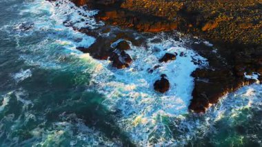 Okyanus dalgalarının yukarıdan görünüşü muhteşem kayaların ve kayalıkların etrafında köpürüyor. İlham verici ve inanılmaz doğa konsepti. Destansı sahil şeridinde güçlü deniz suyunun insansız hava aracı çekimi. Yüksek kalite 4k görüntü