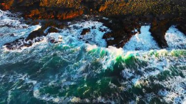 Okyanus dalgalarının yukarıdan görünüşü muhteşem kayaların ve kayalıkların etrafında köpürüyor. İlham verici ve inanılmaz doğa konsepti. Destansı sahil şeridinde güçlü deniz suyunun insansız hava aracı çekimi. Yüksek kalite 4k görüntü