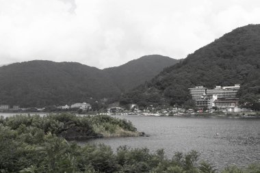 Bunlar Japonya 'da yuva yapmış küçük bir köy olan Fujiyoshida' nın yuvarlanan tepeleri. Bulutlar yanlarından süzülüyor gibi görünüyor. Kawaguchi Gölü aşağıda gösterilir, genellikle sakin görünür..