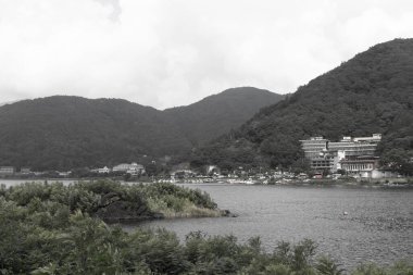 Bunlar Japonya 'da yuva yapmış küçük bir köy olan Fujiyoshida' nın yuvarlanan tepeleri. Bulutlar yanlarından süzülüyor gibi görünüyor. Kawaguchi Gölü aşağıda gösterilir, genellikle sakin görünür..