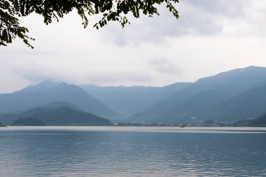 Bunlar Japonya 'da yuva yapmış küçük bir köy olan Fujiyoshida' nın yuvarlanan tepeleri. Bulutlar yanlarından süzülüyor gibi görünüyor. Kawaguchi Gölü aşağıda gösterilir, genellikle sakin görünür..
