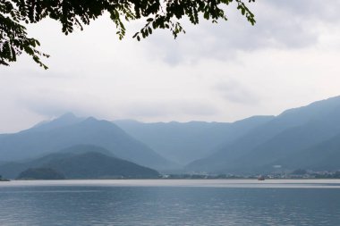 Bunlar Japonya 'da yuva yapmış küçük bir köy olan Fujiyoshida' nın yuvarlanan tepeleri. Bulutlar yanlarından süzülüyor gibi görünüyor. Kawaguchi Gölü aşağıda gösterilir, genellikle sakin görünür..