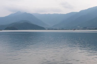 Bunlar Japonya 'da yuva yapmış küçük bir köy olan Fujiyoshida' nın yuvarlanan tepeleri. Bulutlar yanlarından süzülüyor gibi görünüyor. Kawaguchi Gölü aşağıda gösterilir, genellikle sakin görünür..