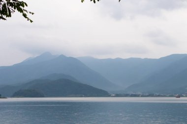 Bunlar Japonya 'da yuva yapmış küçük bir köy olan Fujiyoshida' nın yuvarlanan tepeleri. Bulutlar yanlarından süzülüyor gibi görünüyor. Kawaguchi Gölü aşağıda gösterilir, genellikle sakin görünür..