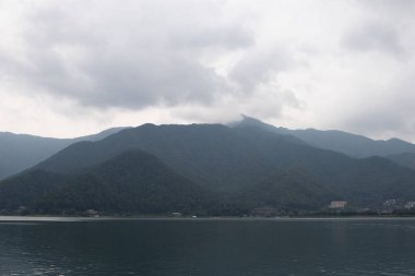 Bunlar Japonya 'da yuva yapmış küçük bir köy olan Fujiyoshida' nın yuvarlanan tepeleri. Bulutlar yanlarından süzülüyor gibi görünüyor. Kawaguchi Gölü aşağıda gösterilir, genellikle sakin görünür..