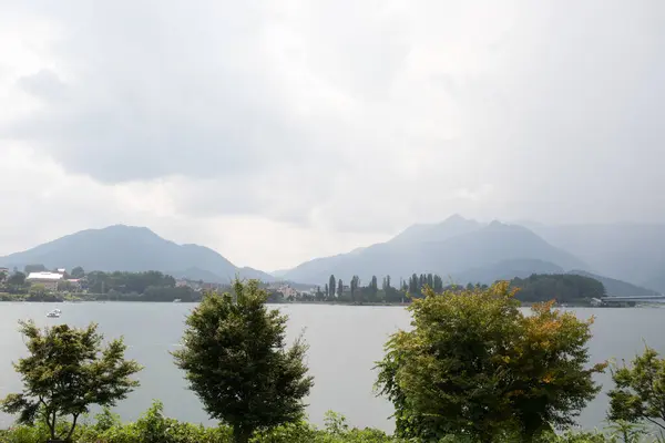 Bunlar Japonya 'da yuva yapmış küçük bir köy olan Fujiyoshida' nın yuvarlanan tepeleri. Bulutlar yanlarından süzülüyor gibi görünüyor. Kawaguchi Gölü aşağıda gösterilir, genellikle sakin görünür..