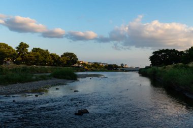 Bu güzel kanal Kyoto Japonya 'dan geçiyordu. Yansıtıcı su çok güzel görünüyor. Yeşil yapraklar ve bir yürüyüş yolu kıyı şeridinde görülebilir. Kabarık beyaz bulutlar gökyüzünde yüksekte.