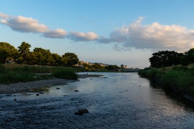 Bu güzel kanal Kyoto Japonya 'dan geçiyordu. Yansıtıcı su çok güzel görünüyor. Yeşil yapraklar ve bir yürüyüş yolu kıyı şeridinde görülebilir. Kabarık beyaz bulutlar gökyüzünde yüksekte.